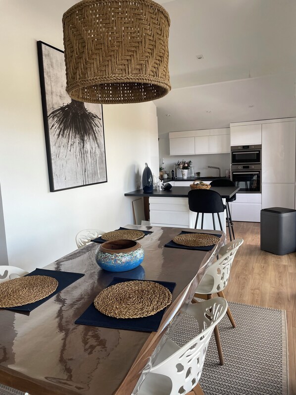 A modern dining area with a long table, woven placemats, and a hanging light fixture.