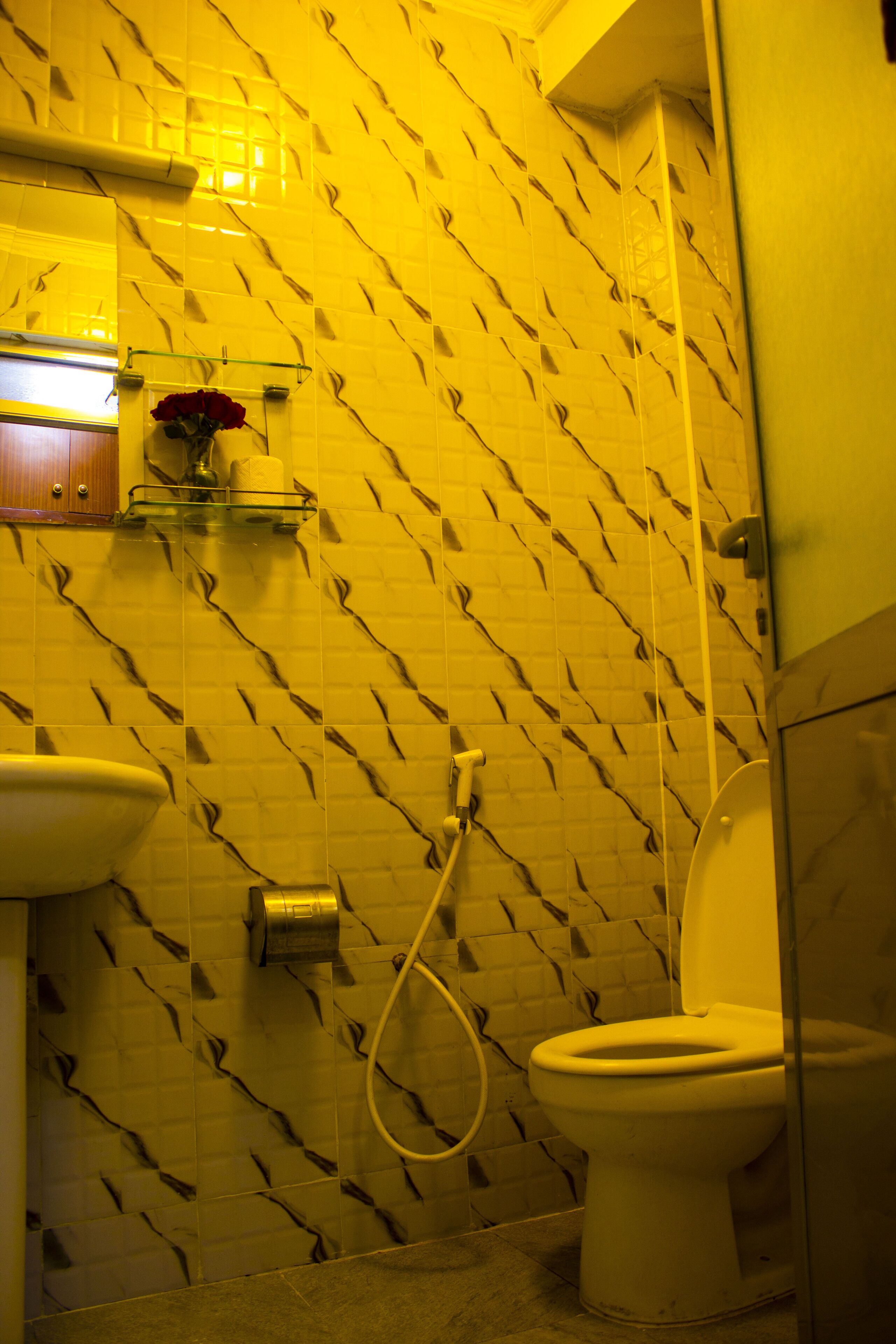 A bathroom with a patterned tile wall, a toilet, a sink, and a glass shelf with a vase.