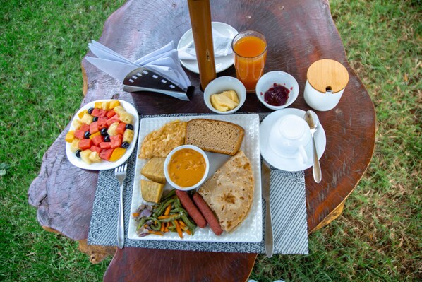 A picnic setup with food items on a wooden table outdoors. - New Hotel Aquiline (Arusha)