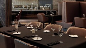 A modern dining area with a long table set for a meal, cushioned seating, and a kitchen in the background. - Great Canadian Casino Resort Toronto (Toronto)