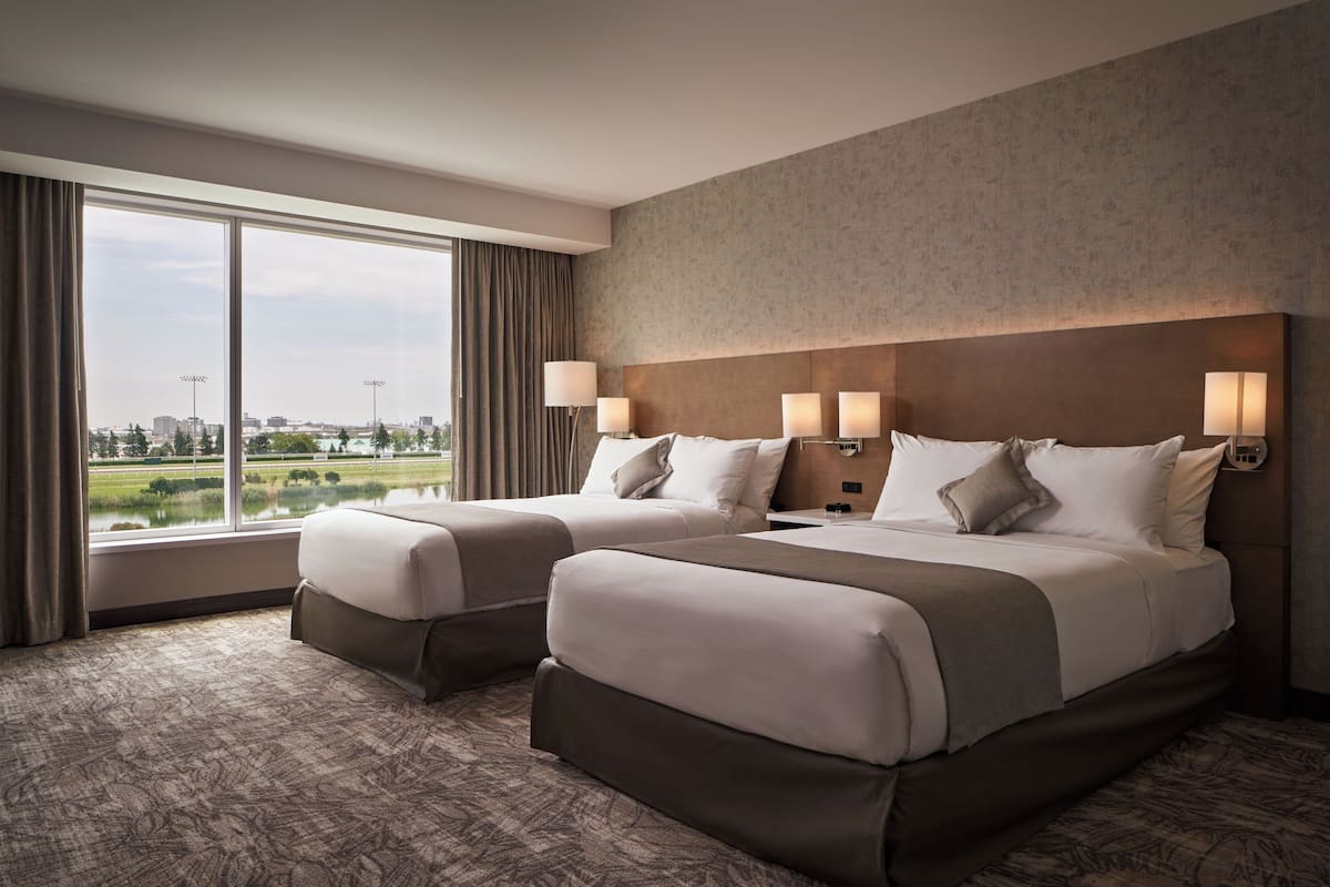 A hotel room with two beds, large windows, and a view of a cityscape and park.
