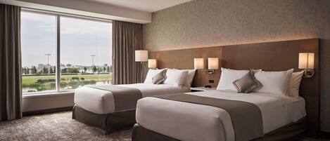 Habitación de hotel con dos camas, ventanas amplias y vistas a la ciudad y un parque.