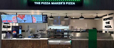 A pizza restaurant with a sign reading 'PIZZAIOLO THE PIZZA MAKER'S PIZZA' and a menu board above the counter.