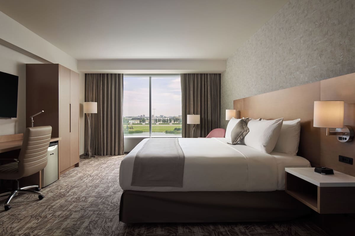 A hotel room with a large bed, a desk, a chair, and a view of the city.