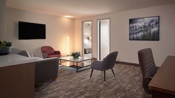A modern hotel room with a flat-screen TV, a sofa, a desk, and a coffee table.
