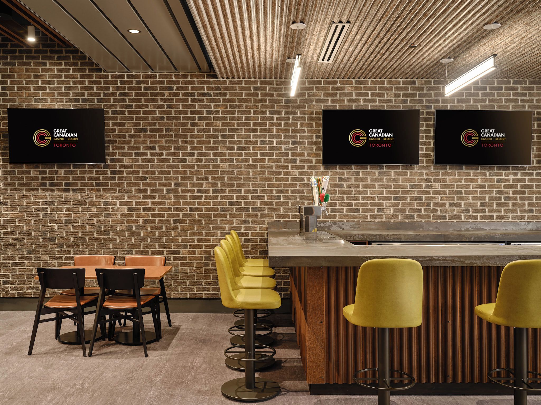 A bar area with a brick wall, bar stools, and a counter.