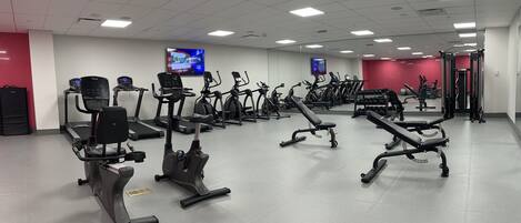 A gym with various exercise equipment, including treadmills and elliptical machines, arranged in rows.