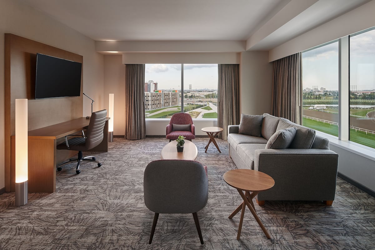 A modern hotel room with a large window, a flat-screen TV, a desk, a sofa, and a coffee table.