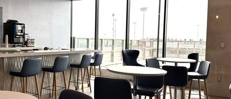 A modern cafe with a geometric ceiling design, large windows offering a view of the city, and a bar area with stools and a coffee machine.