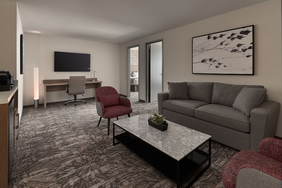 A modern living room with a grey sofa, a red armchair, a coffee table, a flat-screen TV, and a desk with a chair.