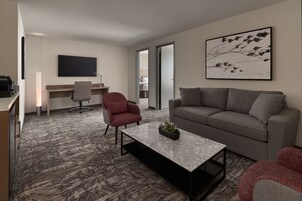A modern living room with a grey sofa, a red armchair, a coffee table, a flat-screen TV, and a desk with a chair.