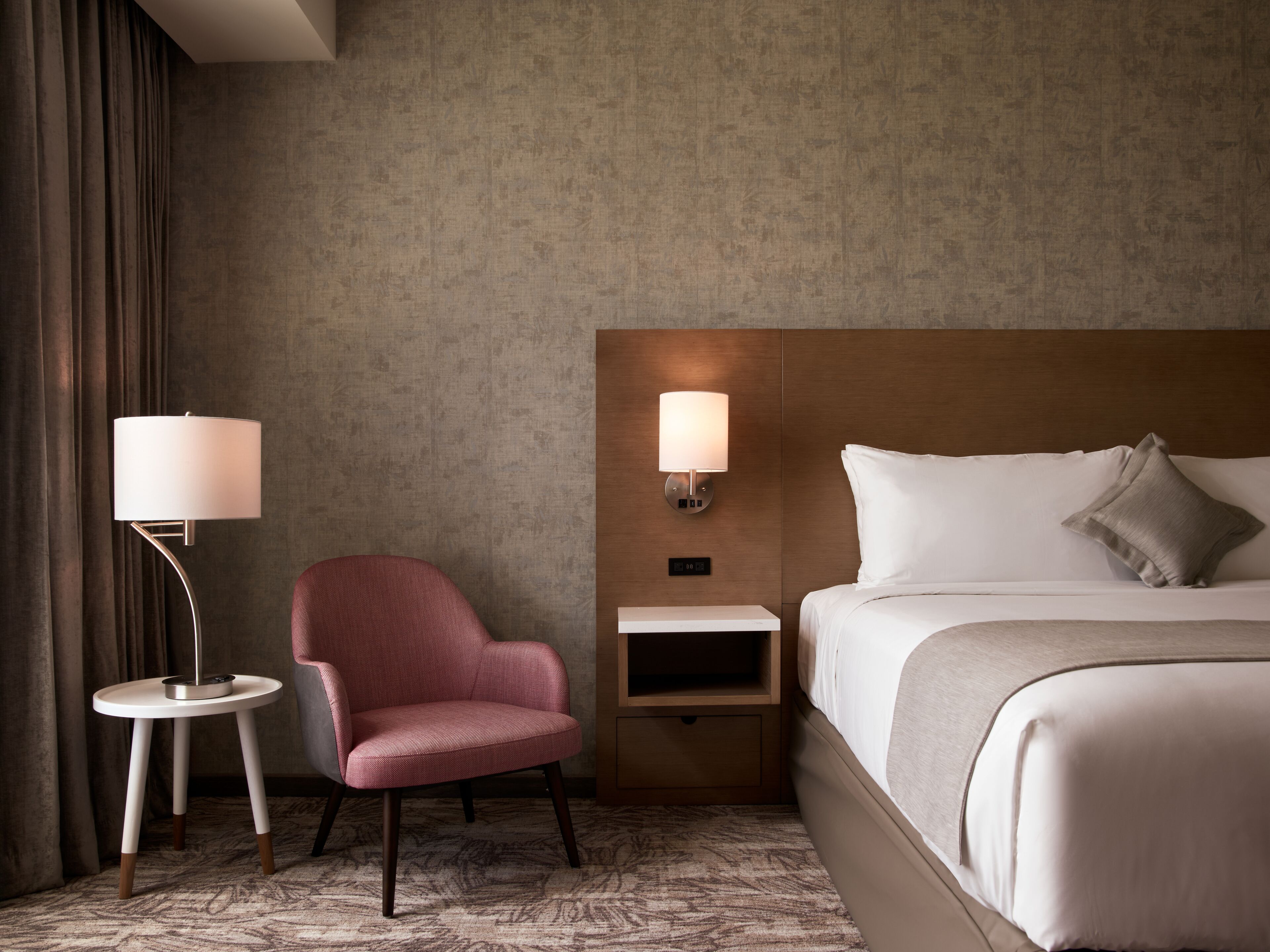 A hotel room with a bed, a nightstand, a lamp, and a chair.