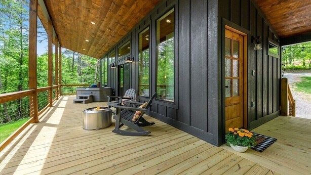 A covered outdoor deck with a fire pit, seating, and a view of the forest. - Dream Big in this new Tiny Home! Hot tub, firepit (Mineral Bluff)