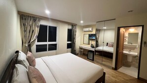 A hotel room with a large bed, a desk with a chair, a TV, a mirror, and a bathroom with a sink and toilet. - V Check Inn Sukhumvit 22 (Bangkok)