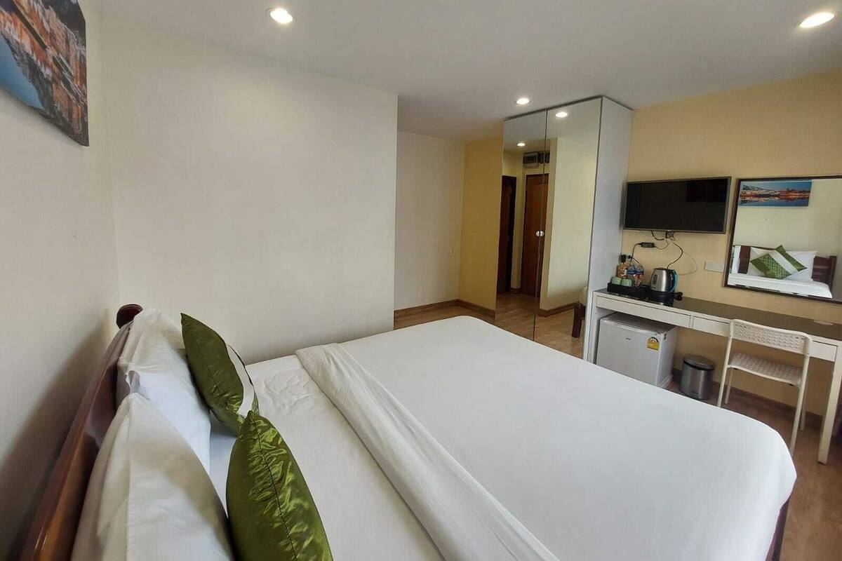 A hotel room with a bed, a desk, a mirror, and a television.