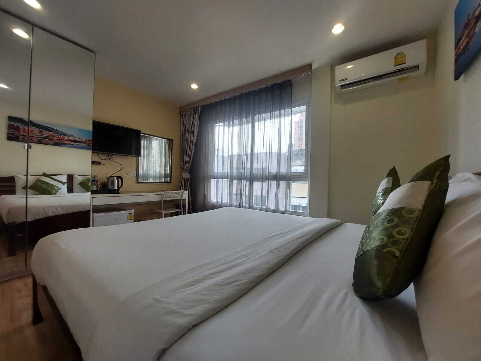 A hotel room with a bed, a desk, a chair, a TV, and an air conditioning unit.