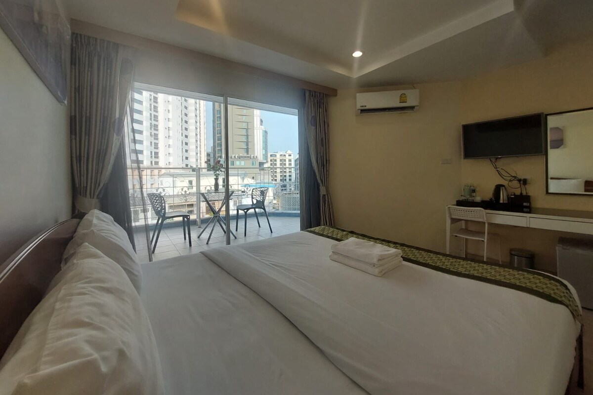 Camera d'hotel con un letto grande, una scrivania, una sedia e un balcone con vista su edifici alti.