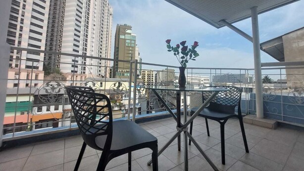 A balcony with two chairs and a table, a vase with flowers, and a cityscape view. - V Check Inn Sukhumvit 22 (Bangkok)