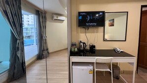 A compact room with a desk, chair, and a small refrigerator. A television is mounted on the wall, and there is a window with curtains. - V Check Inn Sukhumvit 22 (Bangkok)