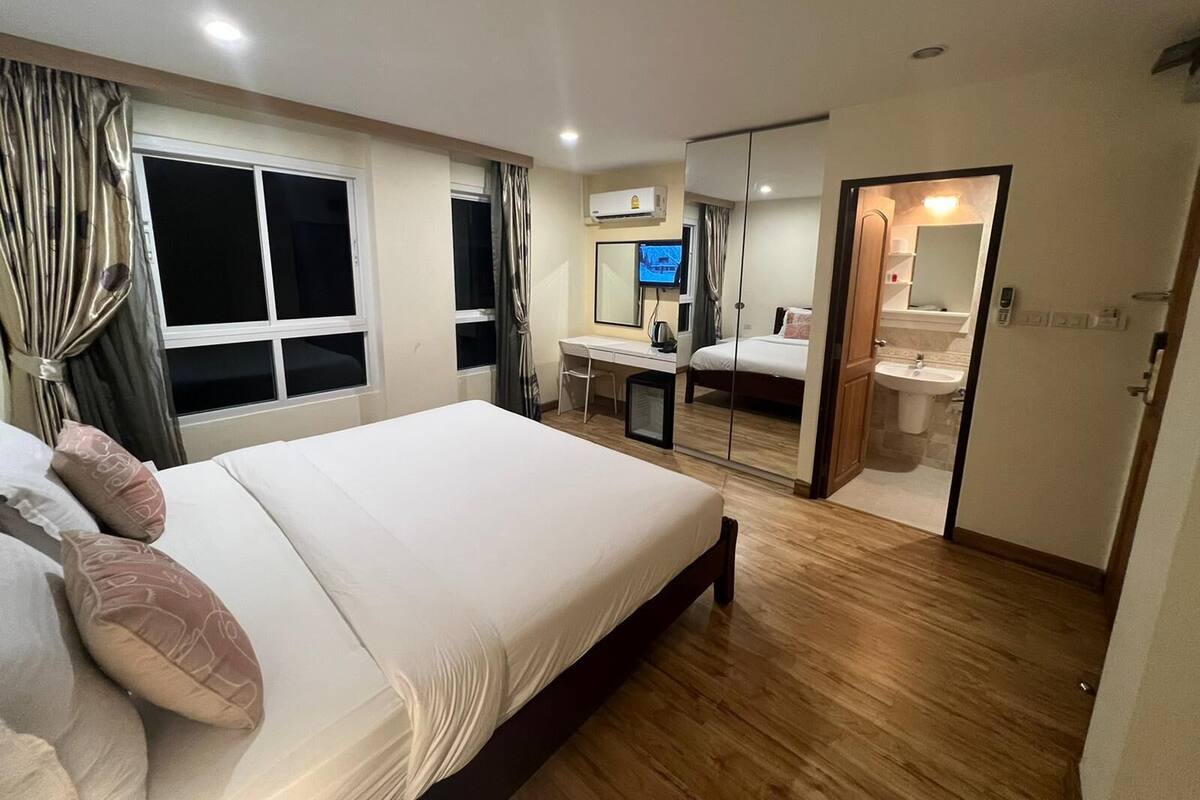 A modern hotel room with a large bed, a desk, a TV, and a bathroom.