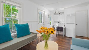 A modern living room with a sofa, a round table with a vase of sunflowers, and a kitchen in the background.