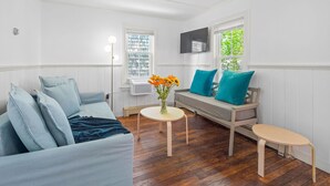 A room with a light blue sofa, a small round table with a vase of flowers, a bench, and a TV mounted on the wall.