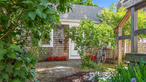 A garden with a wooden fence, a bicycle, and a house with a number 163 sign.
