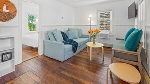 A living room with a light blue sofa, a small round table with a vase of flowers, a wooden chair, and a television mounted on the wall.
