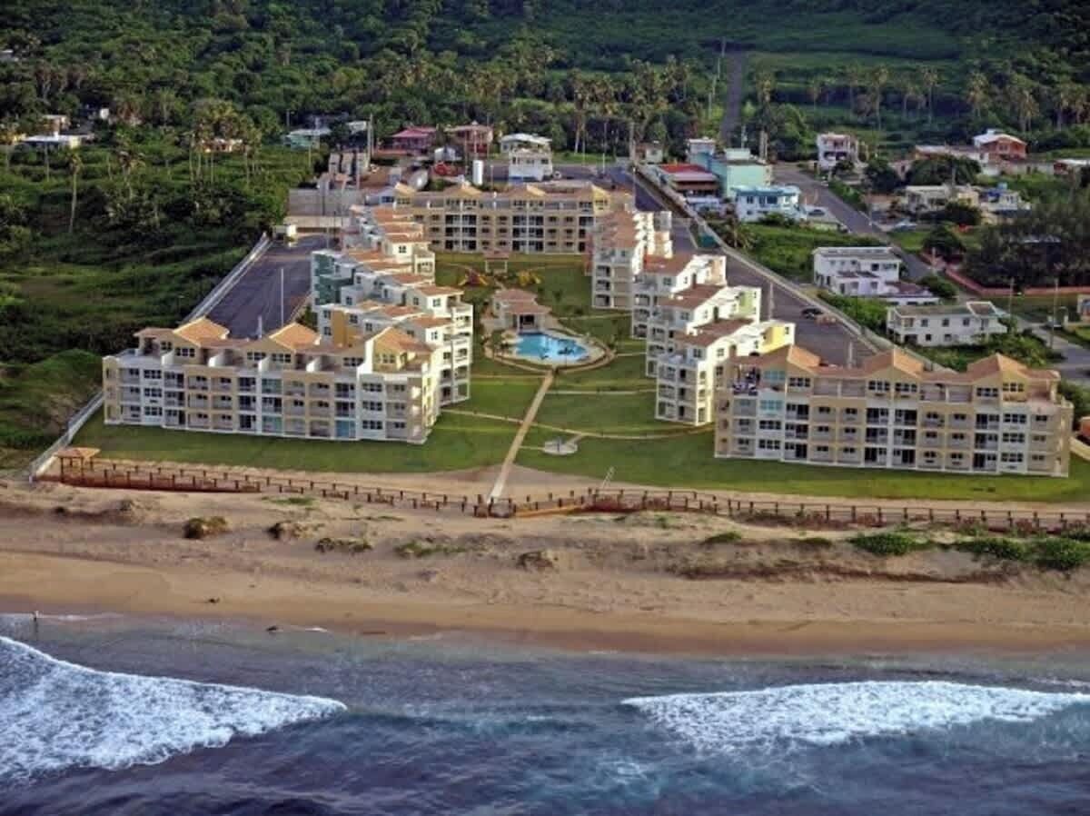 A coastal hotel with multiple buildings, a central pool, and a beach view.