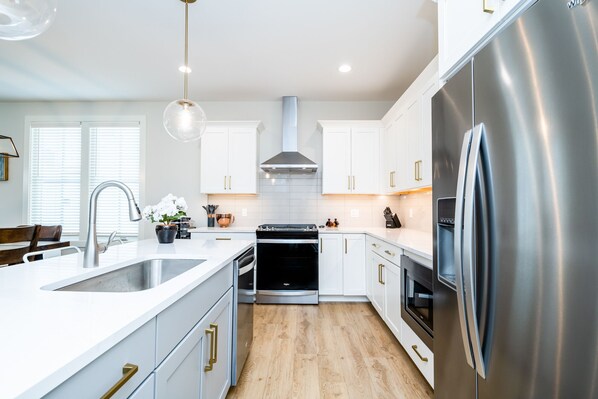 A modern kitchen with white cabinets, stainless steel appliances, and a wooden floor.