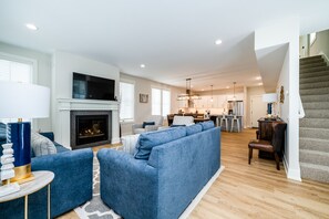 A modern living room with a fireplace, a blue sofa, and a kitchen in the background.