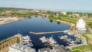 Un port de plaisance où sont amarrés de nombreux bateaux, un pont en arrière-plan et un grand bâtiment avec un toit rouge.