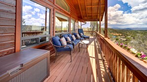 Una terraza de madera con un sofá y sillas, ventanas amplias y vistas al paisaje.
