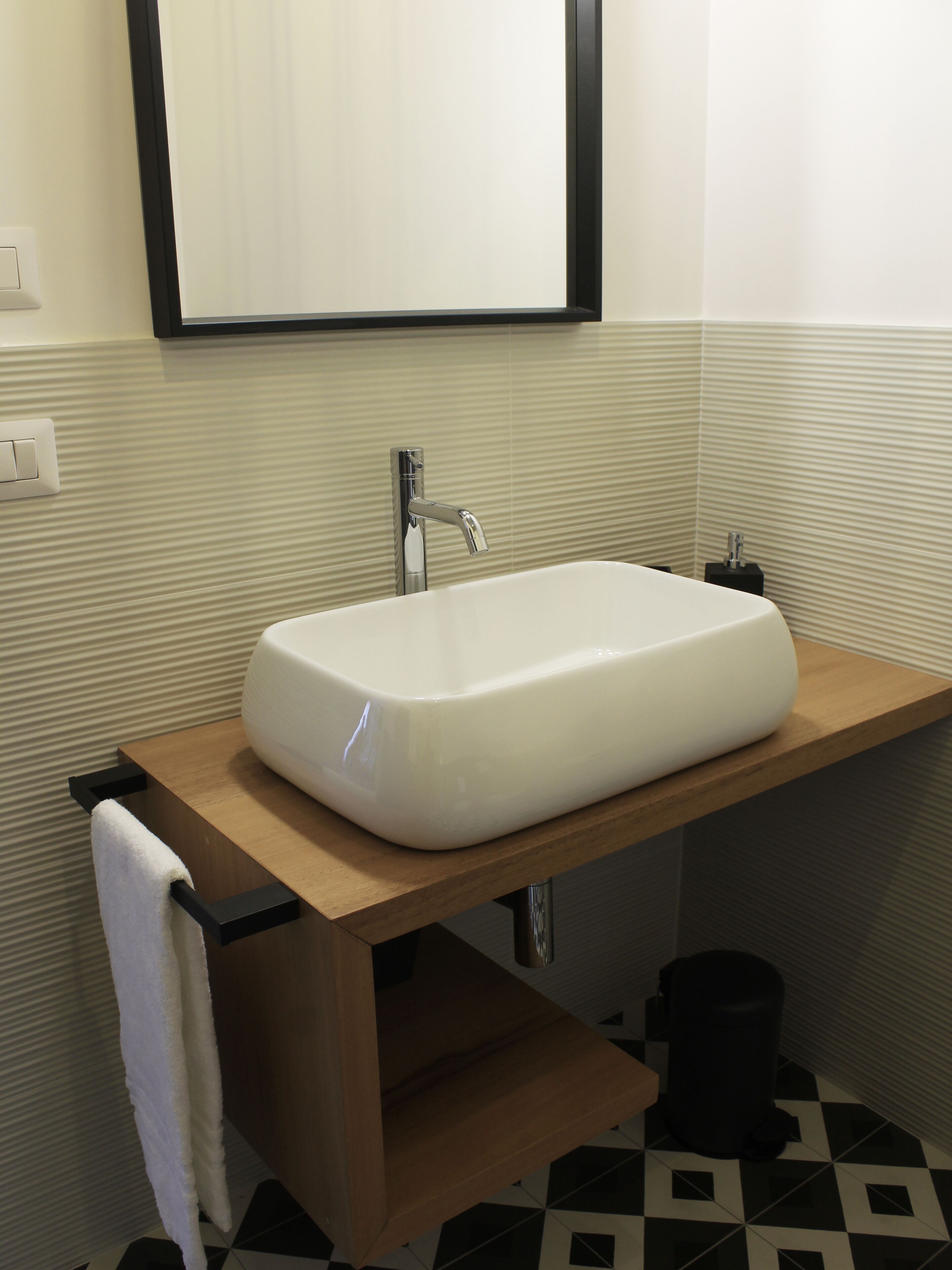 Une salle de bain avec un lavabo blanc, un plan de toilette en bois et une poubelle noire.