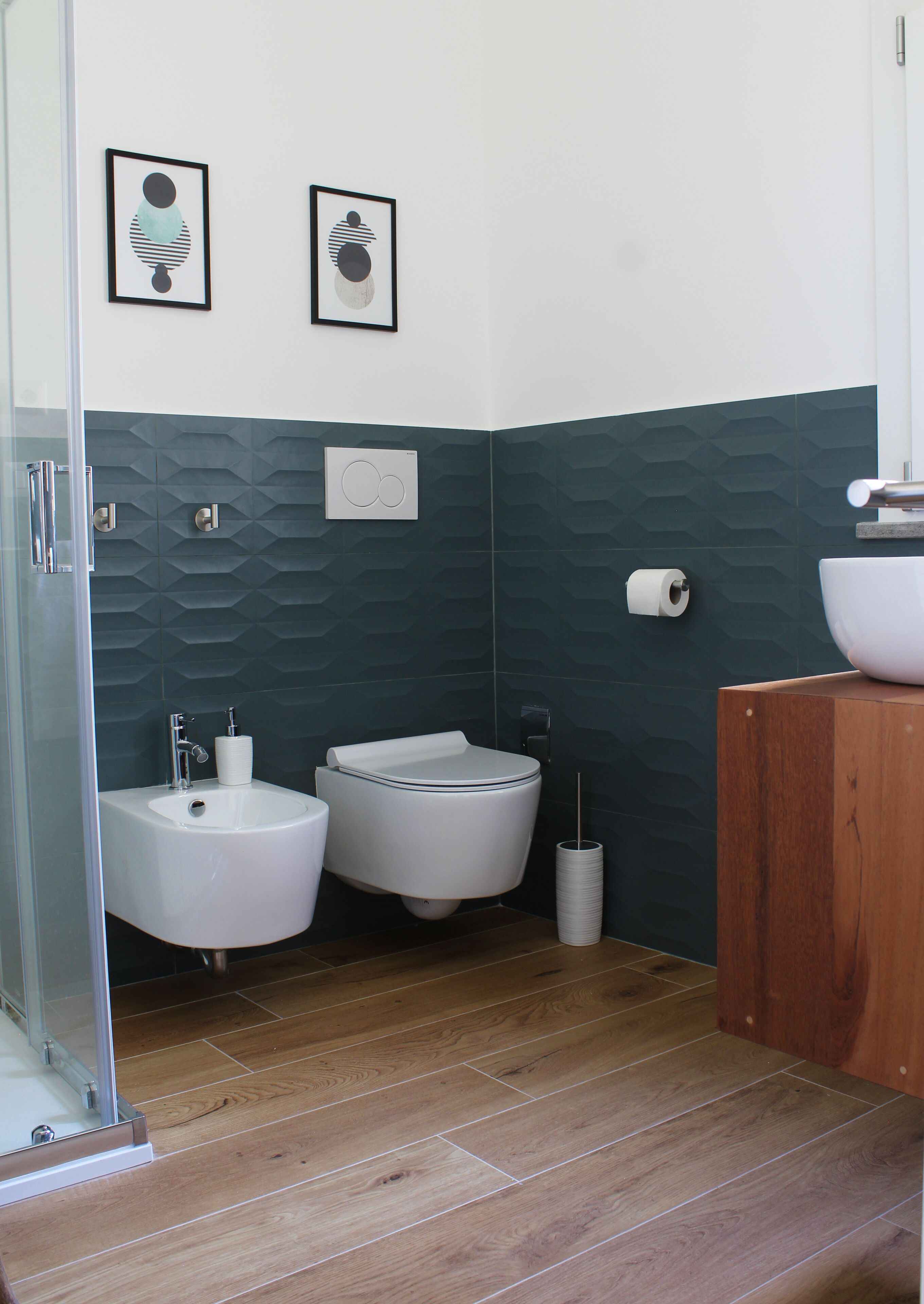 A modern bathroom with a bidet, a sink, and a toilet. There are two framed artworks on the wall.