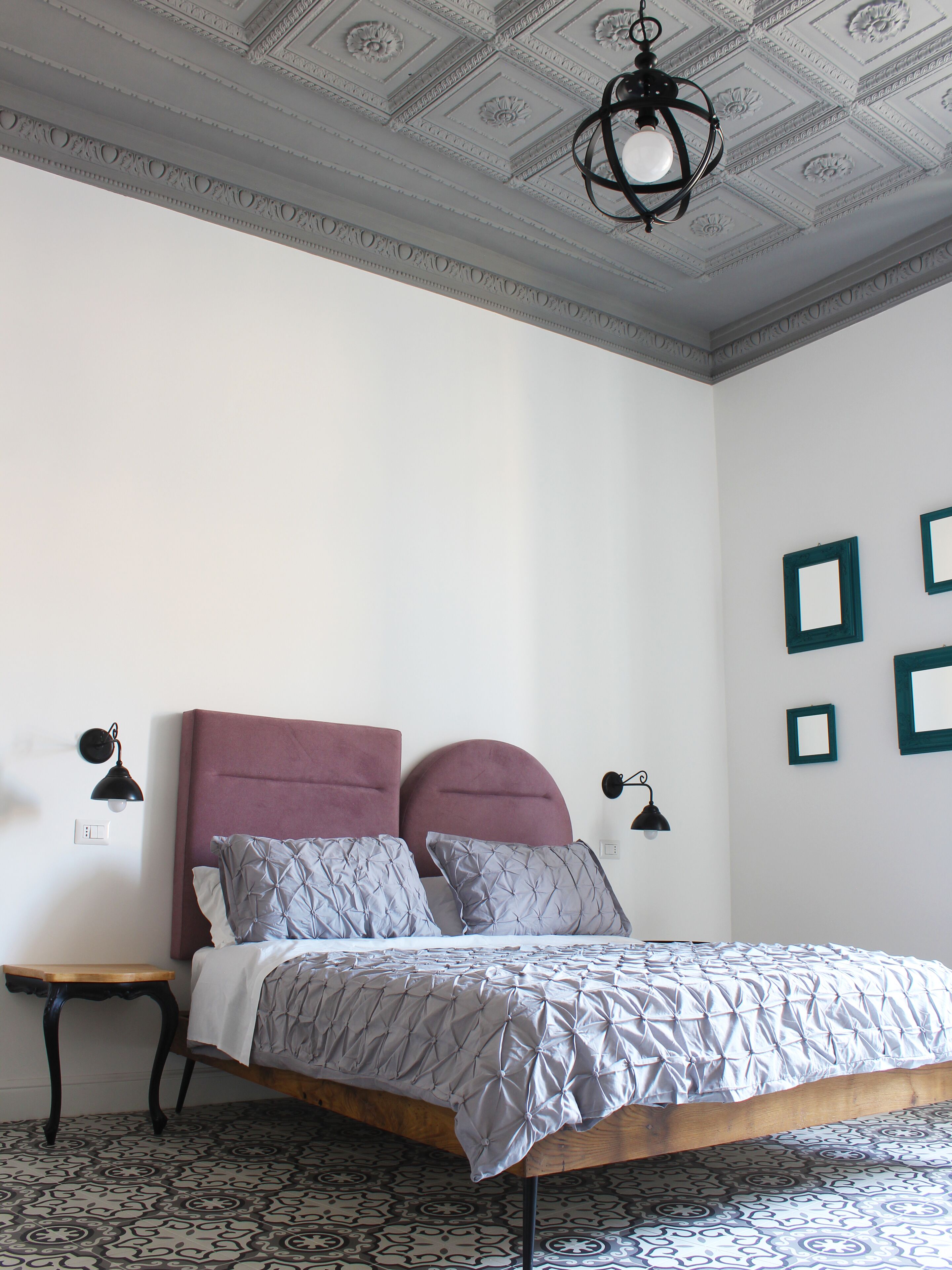 A bedroom with a bed, a nightstand, a ceiling light fixture, and a patterned floor.