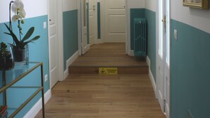 A hallway with wooden flooring, white and teal walls, and several doors leading to rooms. There are framed pictures on the walls and a potted plant on a table. - Ottantotto Viterbo (Viterbo)