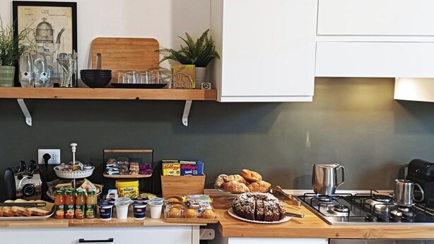 A kitchen with a gas stove, various food items, a coffee maker, and a shelf with plants and kitchenware. - Ottantotto Viterbo (Viterbo)