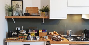 Una cocina con estufa a gas, diversos alimentos, una cafetera y una alacena con plantas y utensilios de cocina.