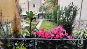 A balcony with potted plants, a view of a well-maintained garden, and a building with a tiled roof. - Ottantotto Viterbo (Viterbo)