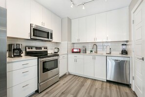 Eine moderne Küche mit weißen Schränken, Edelstahlgeräten, einer Mikrowelle, einem Backofen und einem Geschirrspüler.