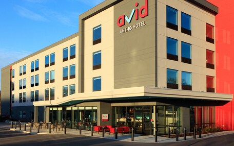 A modern hotel building with a prominent 'avid' sign, multiple windows, and a covered entrance area with seating.