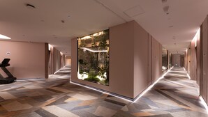 Corredor de hotel com carpete estampado, um equipamento de ginástica e um grande painel iluminado na parede.