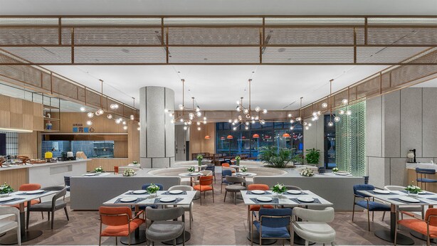 Um restaurante moderno com várias áreas de refeição, um bar central e vista para a paisagem urbana.
