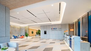 Um lobby moderno com balcão de recepção, área de estar e uma parede com a inscrição 'EXPECT THE UNEXPECTED'.