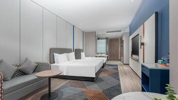 Quarto de hotel moderno com uma cama grande, um sofá, uma pequena mesa redonda e uma televisão.