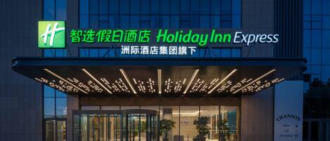A Holiday Inn Express hotel entrance with a glass facade, automatic revolving doors, and a signboard displaying the hotel name and logo.