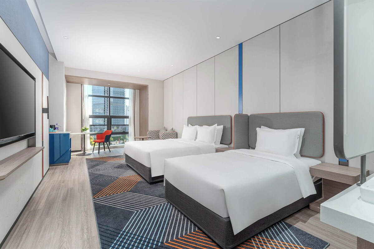 Een hotelkamer met twee bedden, een televisie, een bureau en uitzicht op de stad.
