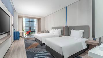 Quarto de hotel com duas camas, televisão, escrivaninha e vista para a cidade.