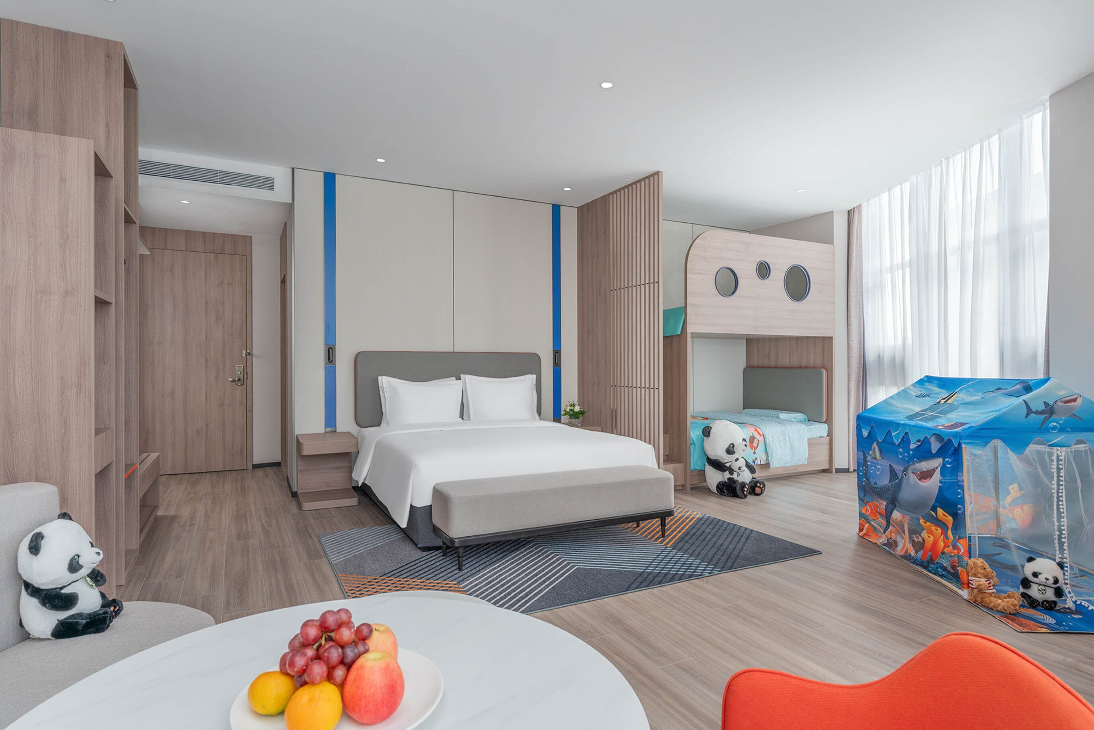 Ein modernes Hotelzimmer mit Bett, Schreibtisch und einer Essecke mit Obst.